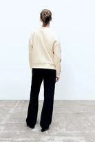 Person in cream-colored girl pattern sweater and black pants, seen from behind