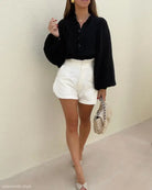 Woman in black lantern sleeve shirt and white shorts, holding a handbag for office wear