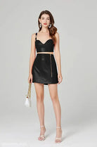 Woman in black elegant leather set featuring a leather chest wrap and zipper hip skirt