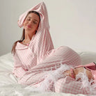 Woman in pink gingham loose satin pajamas stretching on bed, stylish satin pajamas two piece