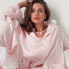 Woman in pink and white gingham loose satin pajamas with pearl necklace and pink heart pendant
