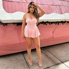 Woman wearing a short pink strapless dress posing against a pink background.