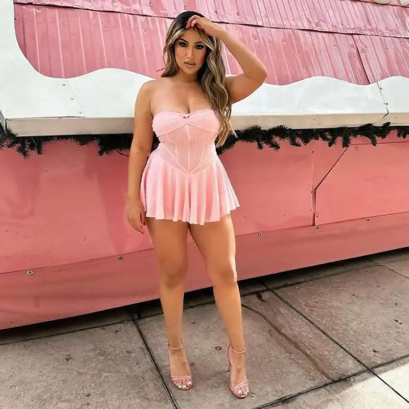 Woman wearing a short pink strapless dress posing against a pink background.